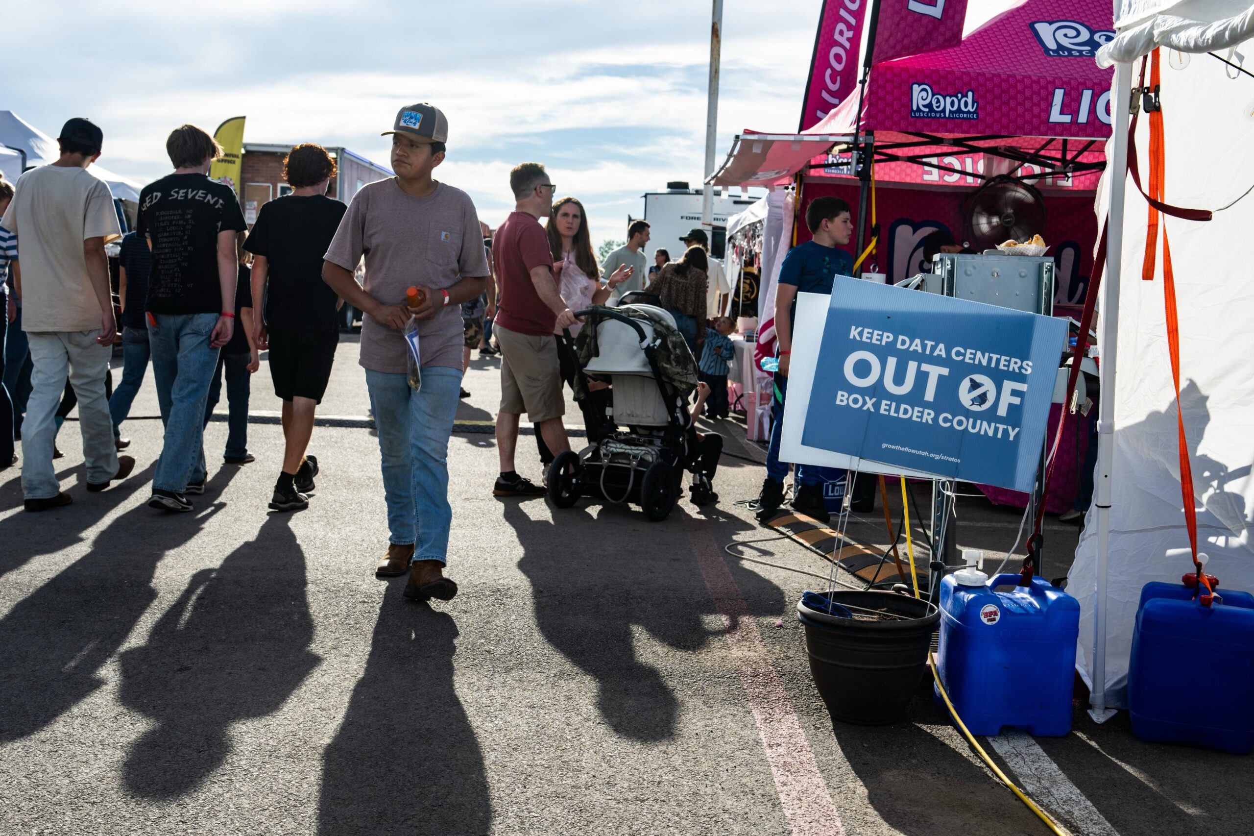 Scene of people walking at a local fair. A sign reads, "Keep data centers out of Box Elder County."
