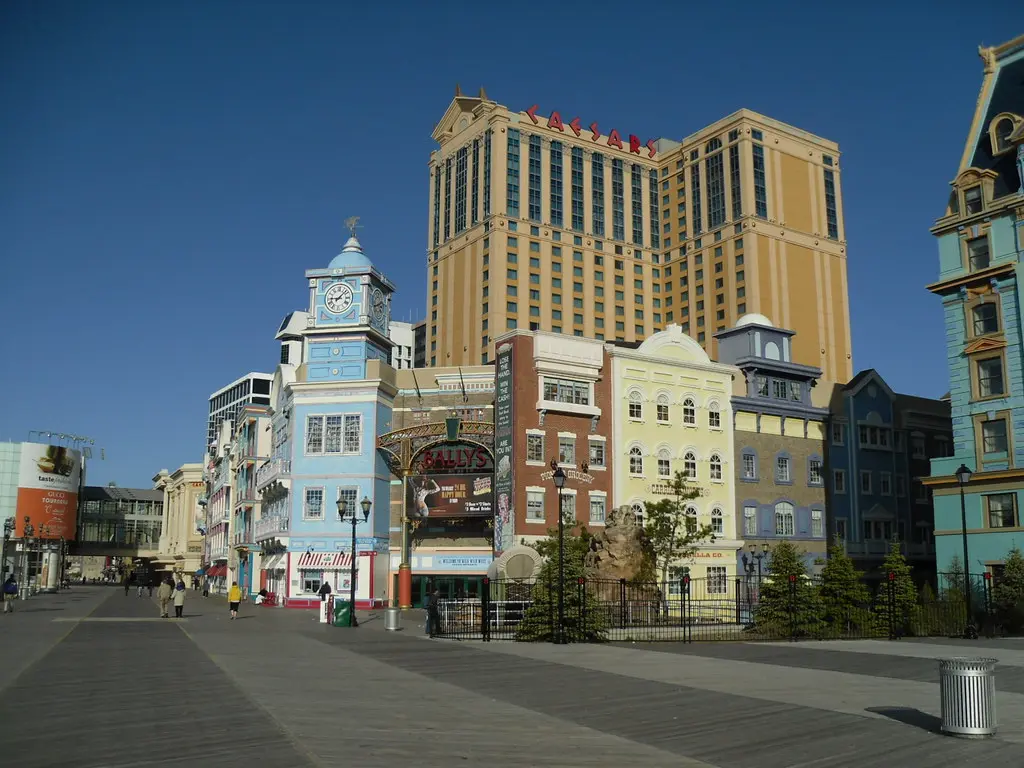 A view of the Atlantic City boardwalk featuring colorful buildings and the Caesars casino hotel in the background.