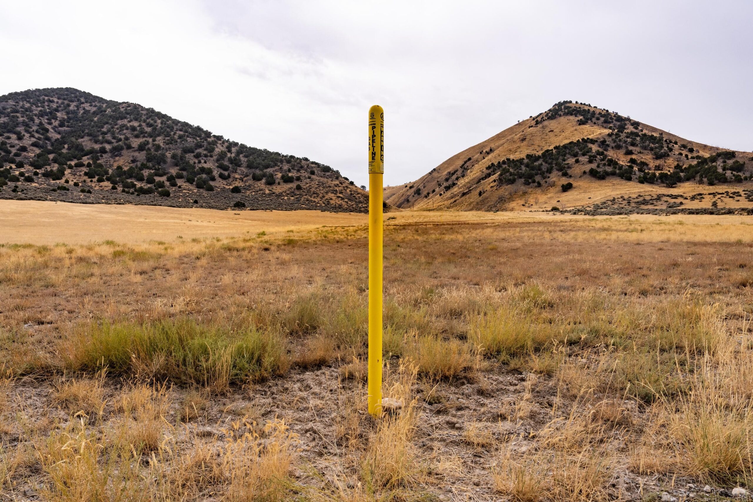 Yellow marker demarcating the Ruby Pipeline on a prairie with hills in the distance.