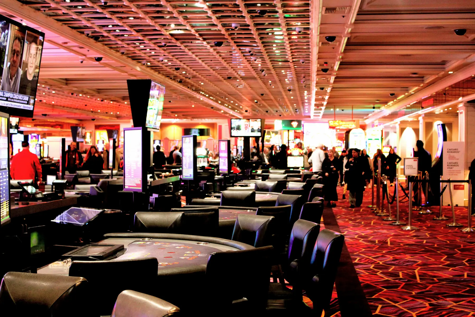 A wide view of a busy casino floor with gaming tables and people walking by.