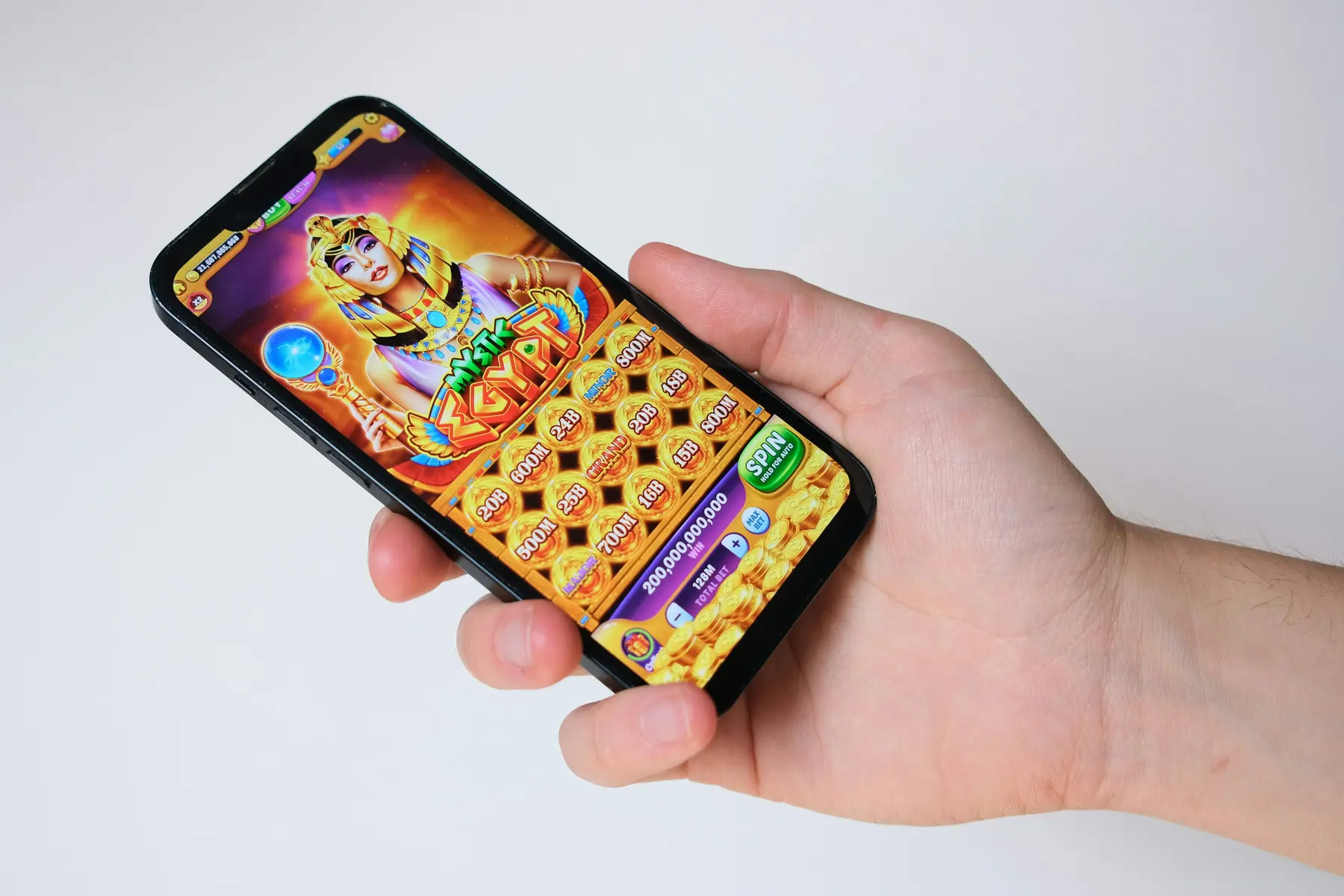 A person's hand holding a smartphone displaying an Egyptian-themed slot machine game