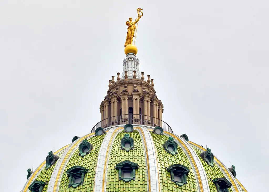 A close-up view of the ornate green and gold dome of the Pennsylvania State Capitol building topped with a golden statue.