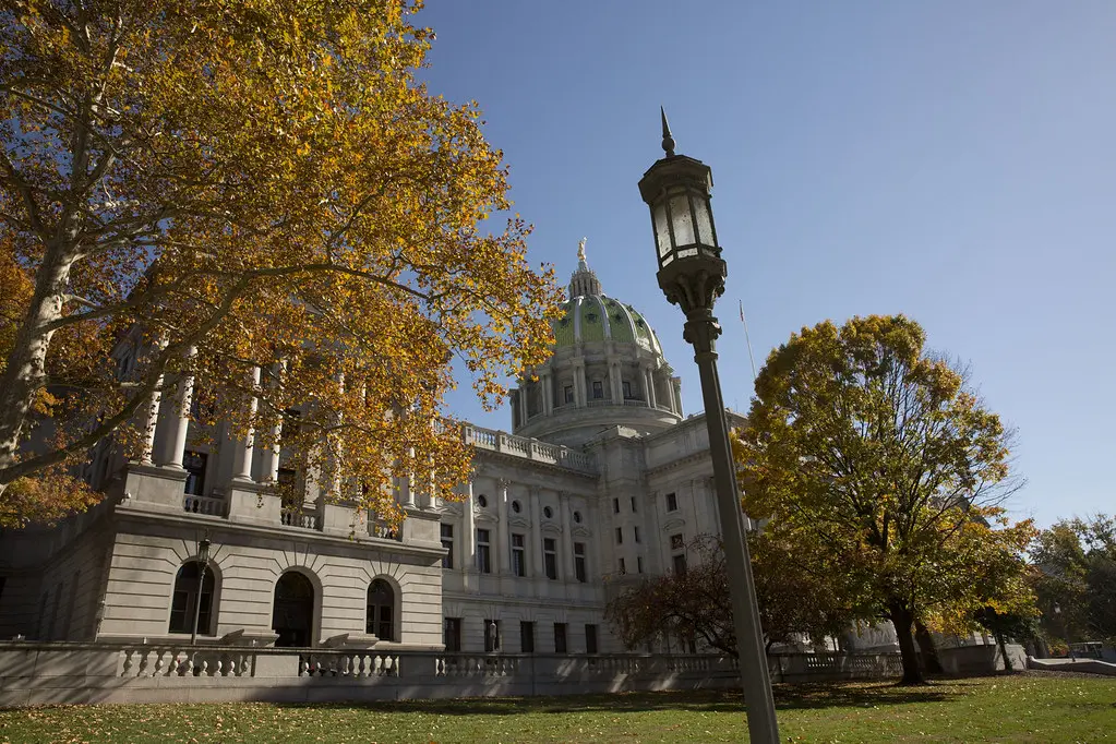 The Pennsylvania State Capitol building with its green dome, framed by yellow autumn leaves.