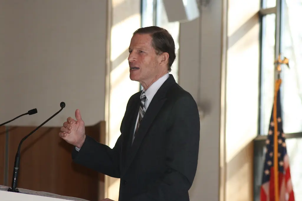 Senator Richard Blumenthal speaking at a podium with an American flag in the background.